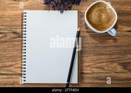 On a wooden table is an open notebook with a pencil on top, a cup of coffee and a bouquet of flowers. Stock Photo