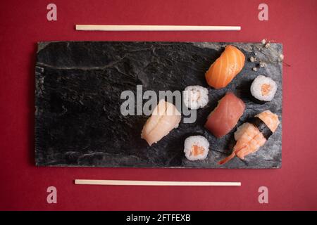 Horizontal photograph with different sushi and a small flower on a black plate with textures and sushi chopsticks. Copy space. Stock Photo