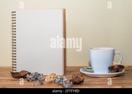 Open spiral notebook with white sheet, coffee cup next to it and table decorations Stock Photo