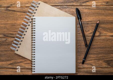 There are spiral notebooks on the wooden table. One open with white sheet with pen and pencil on it. Stock Photo