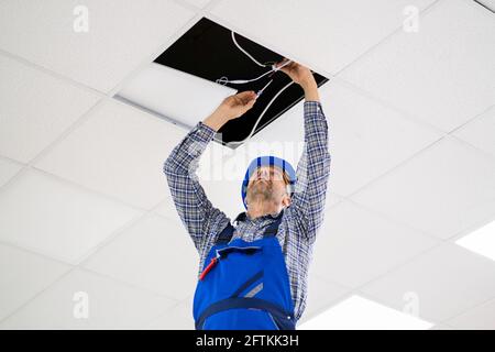 Electrician Installing LED Ceiling Light In Office Stock Photo