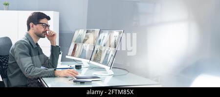 Security System Operator Looking At CCTV Footage At Desk In Office Stock Photo