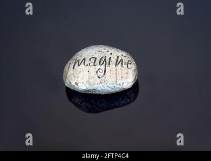 Painted rock imagine word on a shiny black background.  The rock is a metallic silver color, great for concepts and ideas creativity and imagination. Stock Photo