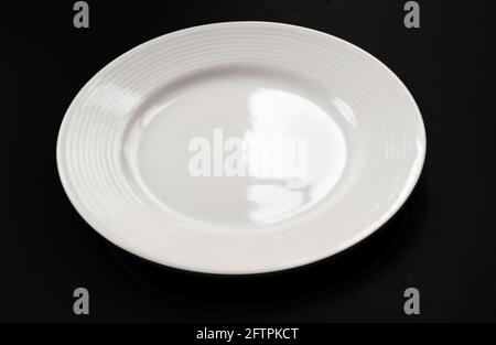 One white plate on black background closeup.  This clean white glass empty dish is a glass object with light reflecting with no food. Stock Photo