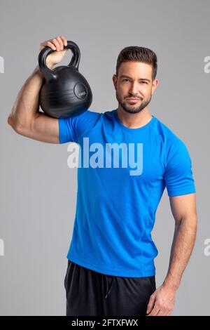 Young sporty fit 30s caucasian man posing with kettlebell on grey background Stock Photo