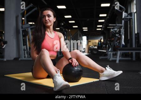 Beautiful athletic woman resting after doing sit ups with medicine ball at sports studio Stock Photo