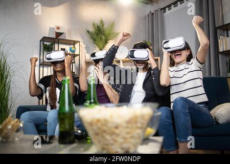 Cheerful diverse people wearing wireless virtual glasses and having fun together at home. Concept of friendship, entertainment and portable digital technology. Stock Photo