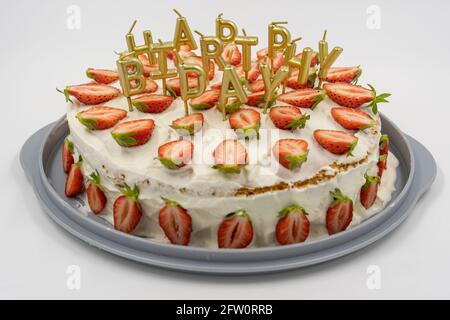 Isolated strawberry cheesecake on white background decorates with golden candles as happy birthday letters. Stock Photo
