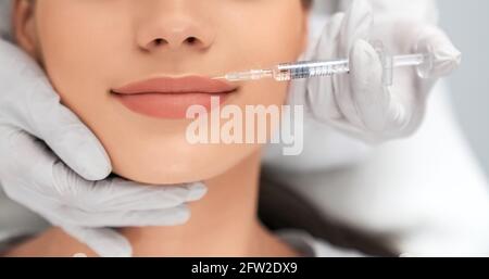 Close up of beautician in white rubber gloves doing injection in lips for young beautiful woman. Concept of process augmentation and improvement lips in professional salon.  Stock Photo