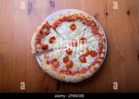Overhead photo of a pizza with a cut slice on a wooden table Stock Photo