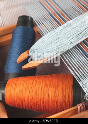 Shuttle with blue thread and two bobbins with indigo and orange yarns for weaving striped textile, upright format Stock Photo