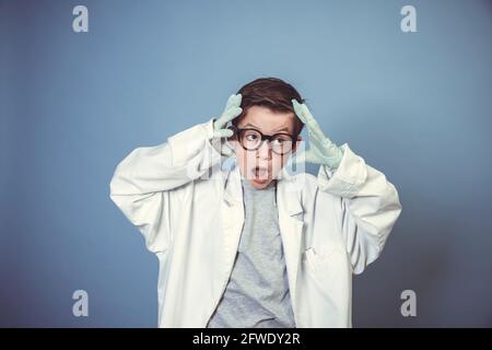 cool school boy with thick black glasses is dressed as mad scientist with white coat in front of blue background Stock Photo