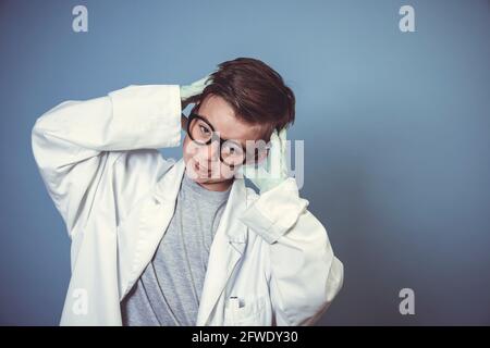 cool school boy with thick black glasses is dressed as mad scientist with white coat in front of blue background Stock Photo