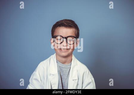 cool school boy with thick black glasses is dressed as mad scientist with white coat in front of blue background Stock Photo