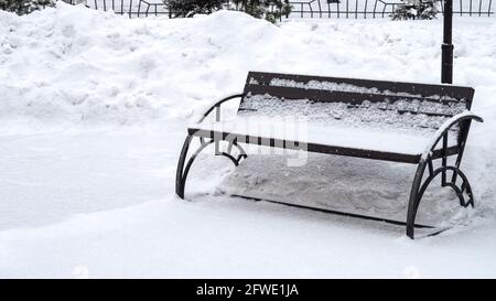 Snow covered empty wooden bench in winter park. Stock Photo