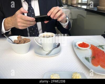 Man in a business suit and tie using smart phone at dining table. He is enjoying social media and breakfast.. Stock Photo