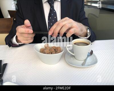 Man in a business suit and tie using smart phone at dining table. He is enjoying social media and breakfast.. Stock Photo