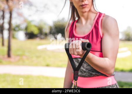 hands of a woman using resistance bands. She is unrecognizable. In a green park. Selective focus in hands Stock Photo