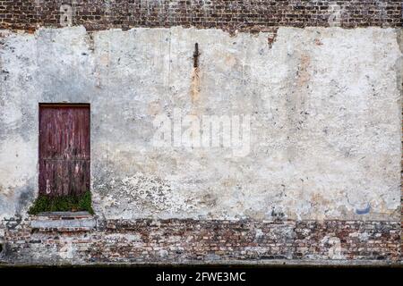 Aged wall painted in white and with a red wooden door that seems abandoned. Stock Photo