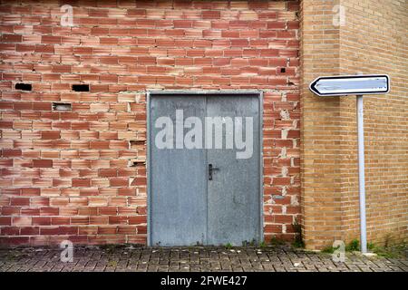 Old orange brick wall with metal sheet door and indicator sign with the inscription erased Stock Photo