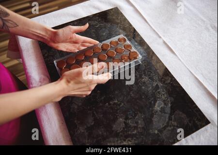 Close-up of female hands holding chocolate molds full of liquid heated chocolate mass. Preparing chocolates for celebrating World Chocolate Day Stock Photo
