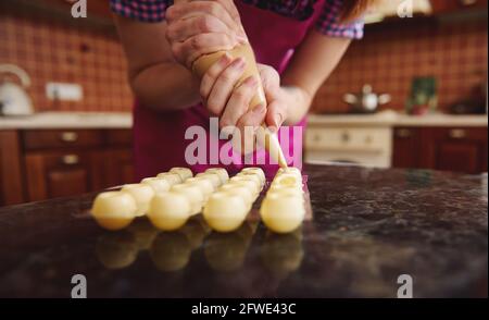 Closeup of chef in pink apron squeezing melted white chocolate with sweet creamy liquid from confectionery bag into harvested candy molds for preparin Stock Photo