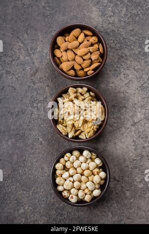 Almonds, walnuts and hazelnuts in wooden bowls on dark concrete background. Top view Stock Photo