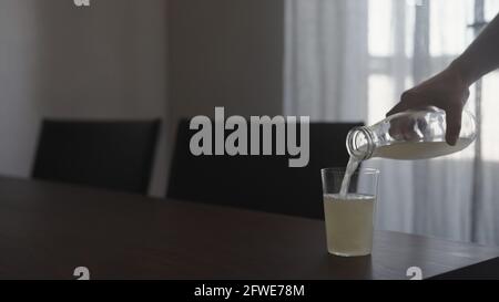 Man pour ginger beer from glass bottle into tumbler glass on walnut table indoor, wide photo Stock Photo