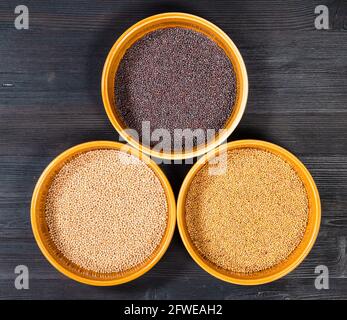 top view of ceramic bowl with various mustard seeds (yellow, black, white) on black wooden table Stock Photo