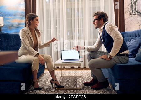 young business couple talking, sitting at the sofa, over the laptop. copy space Stock Photo