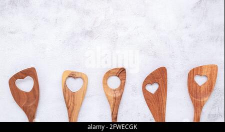 Various heart shape of wooden cooking utensils. Wooden spoons and wooden spatula on white concrete background with flat lay and copy space. Stock Photo