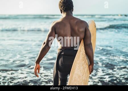 Male afro surfer having fun surfing during sunset time - African man enjoying surf day - Extreme sport lifestyle people concept
