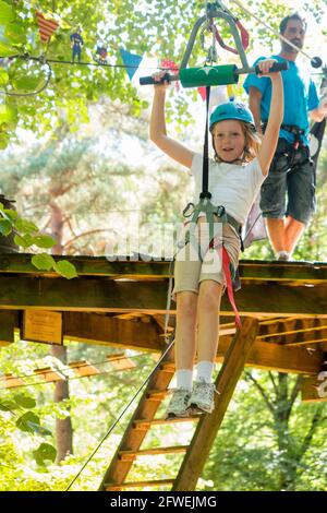 Young girl girls child kid on a children obstacle course zip wire line activity trail high in woodland forest tree, at an adventure park in France during the summer. Rather like a Go Ape adventure experience. (100) Stock Photo