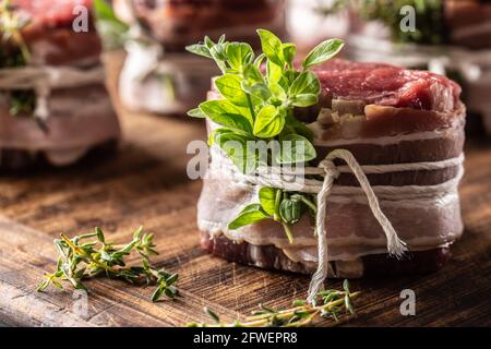Raw steak wrapped with bacon and fresh herbs on a wooden cutting board. Stock Photo