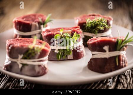 Raw beef steak cuts on a plate wrapped with strings and fresh herbs. Stock Photo