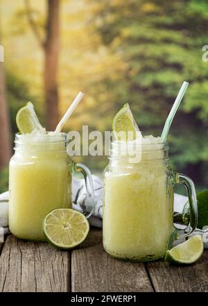 Slush drink with lime in glass jars outside on a wooden table with summer background scene Stock Photo