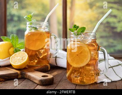 Two drinking glass jars of iced tea with lemon and mint by a window with country background scene Stock Photo