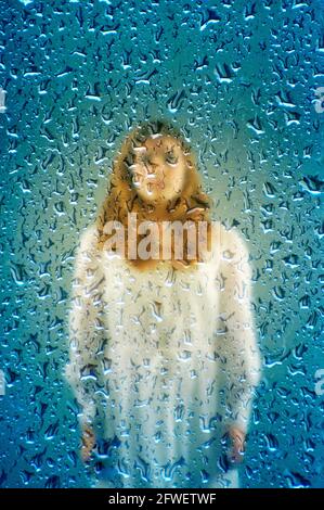 mysterious girl in white dress behind a glass with drops of water Stock Photo