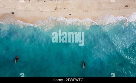 Aerial shot of the white sand beach shore and emerald water with fishermen's boats floating on Indian ocean waves on the Zanzibar island, Tanzania. Stock Photo