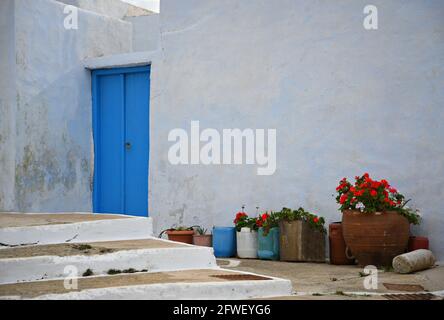 Picturesque rural house facade with a whitewashed wall,  ight blue wooden door clay pots with flowers in Amorgos island, Cyclades Greece Stock Photo