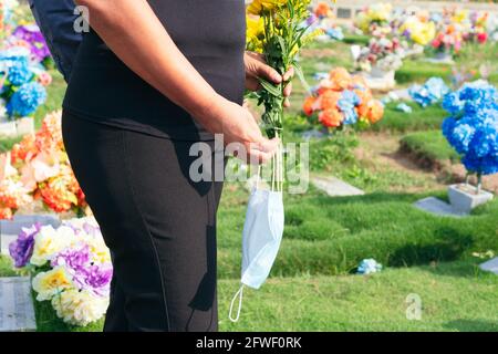 Sad couple with medical mask in cemetery. Mother mourning the loss of her son. Death, graveyard, loss of loved ones due to pandemic. Tragic results of Stock Photo
