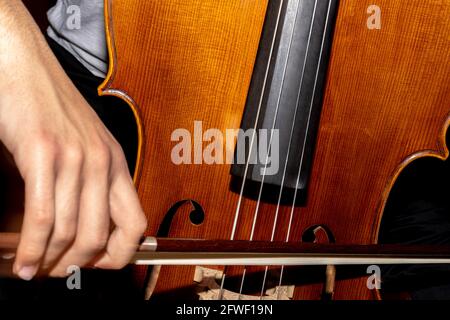 detail of a man playing the wooden cello rubbing the strings with the bow to get the notes of a classical music piece. Stock Photo