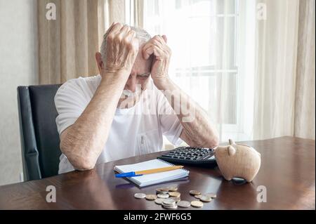 old man in a depression counts pennies from the pension fund. worried elderly man puts money in a piggy bank. impact of lockdown on the economy and th Stock Photo