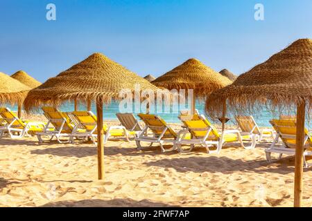 Close view of lounge chairs and parasols on Albufeira beach, Algarve, Portugal. Blue sky and gold sand. Stock Photo