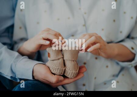 Cropped shot of future woman and man ready to become parents holds childrens shoes. Waiting for infant. Happy family concept Stock Photo