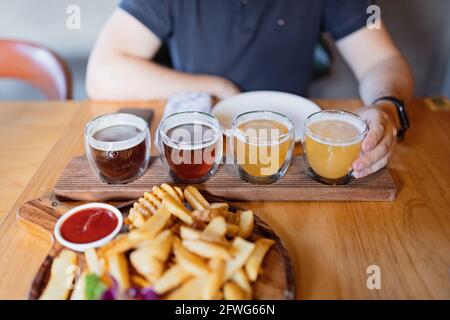Man sampling variety of seasonal craft beer in pub. Beer samplers in small glasses individually placed in holes fashioned into unique wooden tray Stock Photo
