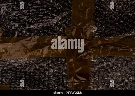 Wrinkled adhesive tape on black bubble wrap. Brown sellotape. Abstract dark background Stock Photo
