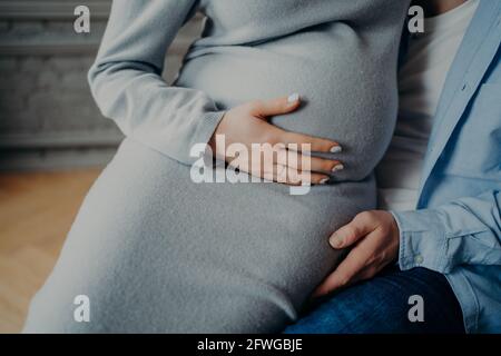Pregnant woman with big belly poses on husbands hands feels child movement in abdomen. Parenthood concept Stock Photo