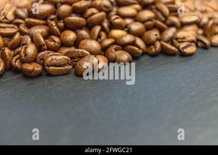 Heap of coffee beans lying on a dark slate desk forming the top edge of a photo. Stock Photo