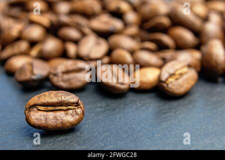 Closeup view of coffee bean lying  in front of heap of coffee beans. Horizontally. Stock Photo